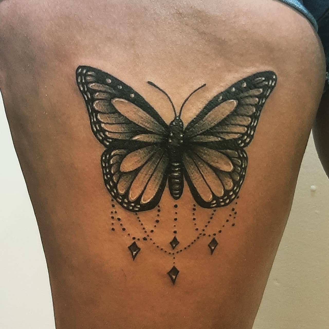 Tatuaje realista de una mariposa en blanco y negro con dijes colgantes sobre la piel