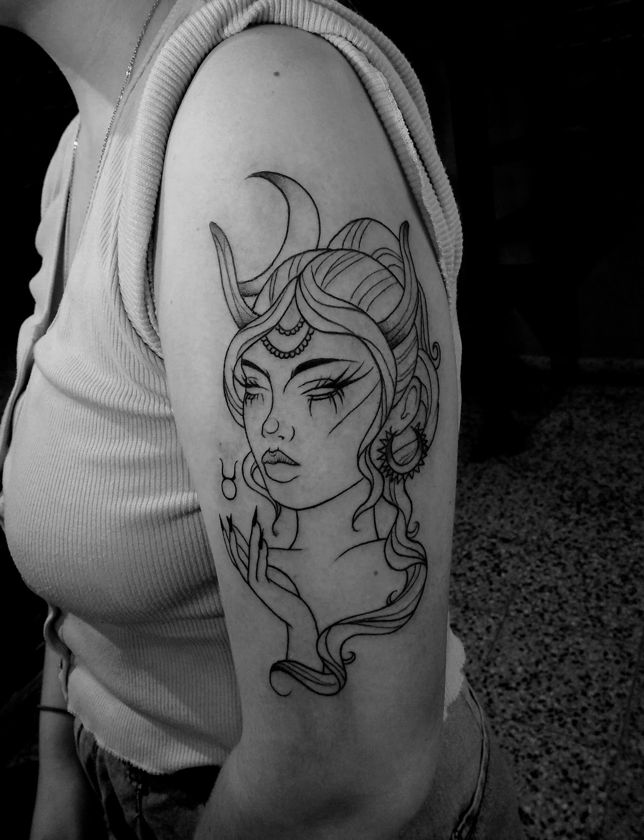 Tatuaje ilustrativo de línea fina de una figura femenina con cuernos y luna sobre el brazo